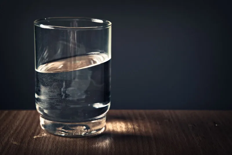 Vaso de agua limpia sobre una mesa de madera con fondo oscuro