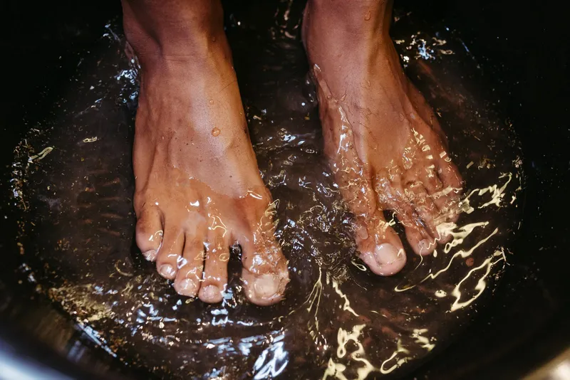 Pies descalzos en remojo en un barreño oscuro con agua y hierbas