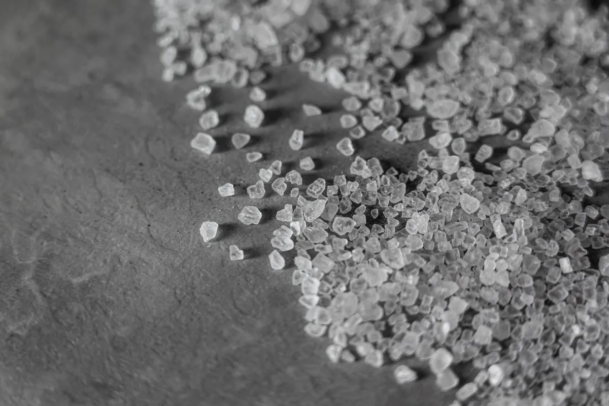 Primer plano en blanco y negro de cristales de sal marina esparcidos sobre una superficie de pizarra.