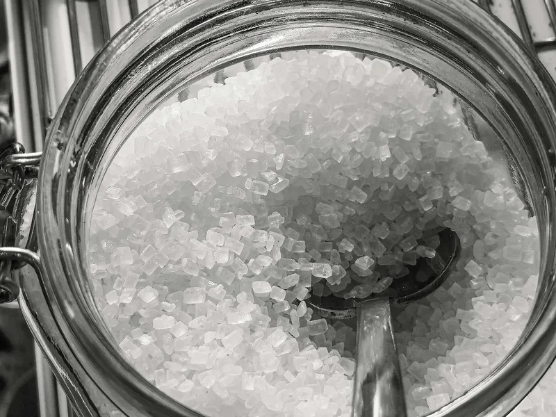 Tarro de cristal lleno de sal marina gruesa con una cuchara metálica en su interior.