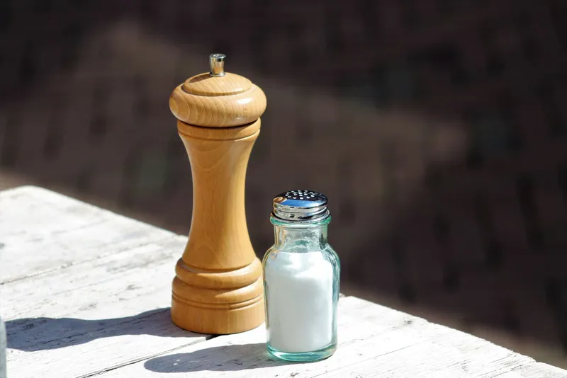 Molinillo de madera y salero de cristal sobre una mesa de madera blanca a pleno sol