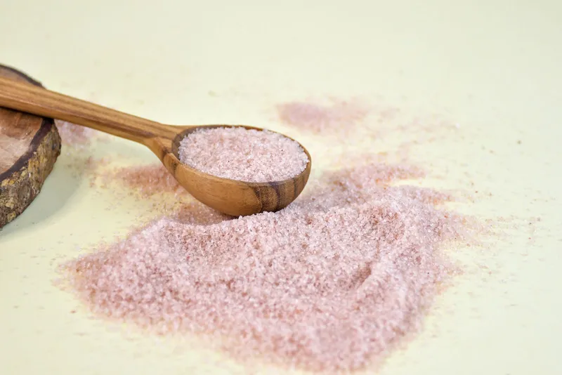 Cuchara de madera con sal rosa del Himalaya derramada sobre una superficie clara