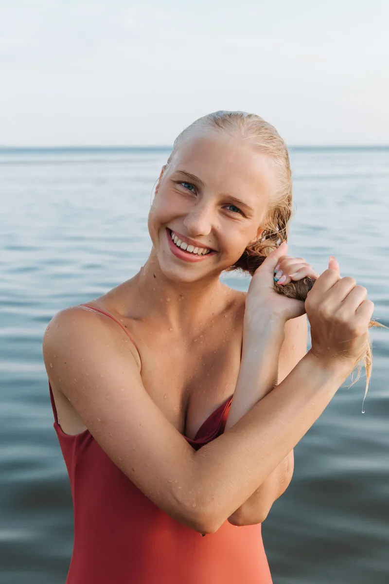 Chica sonriente con el pelo mojado retorciéndolo frente al mar