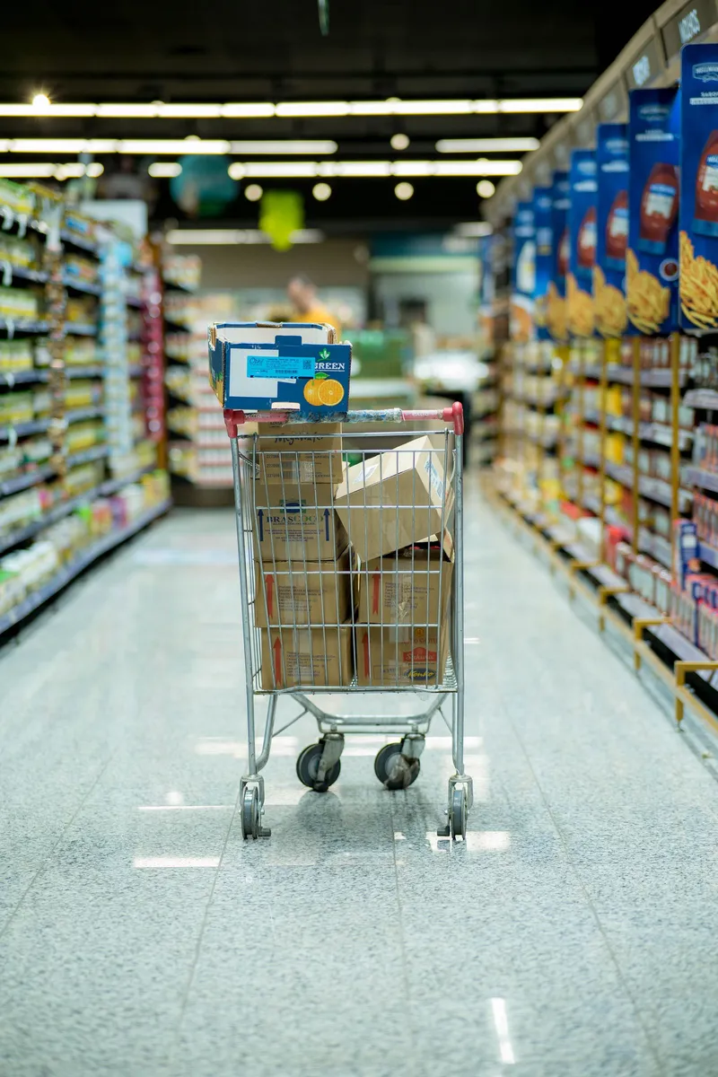 Carro de la compra con cajas de productos en el pasillo de un supermercado.