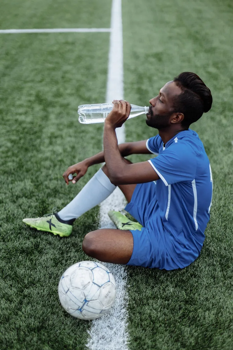 Jugador de fútbol sentado en el césped hidratándose durante un descanso del partido