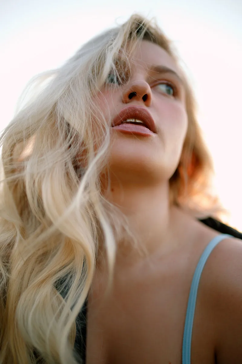 Mujer rubia con ondas de playa en el pelo iluminada por la luz cálida del atardecer